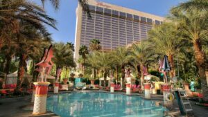 Pool surrounded by flamingo statues and pool deck furniture with a hotel in the background